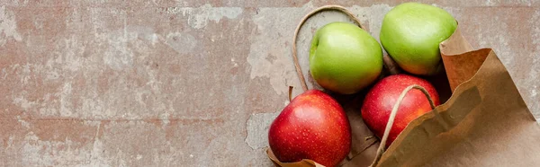 Top view of paper bag with red and green apples on weathered beige surface, panoramic crop — Stock Photo