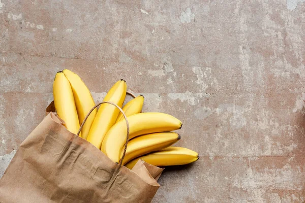 Верхний вид бумажного пакета с бананами на бежевой выветриваемой поверхности — стоковое фото