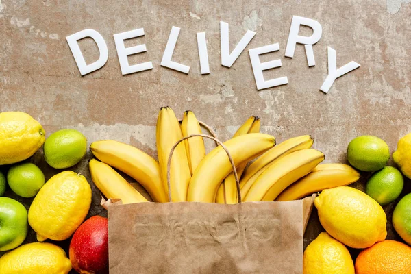 Top view of word delivery near paper bag with colorful fresh fruits on beige weathered surface — Stock Photo