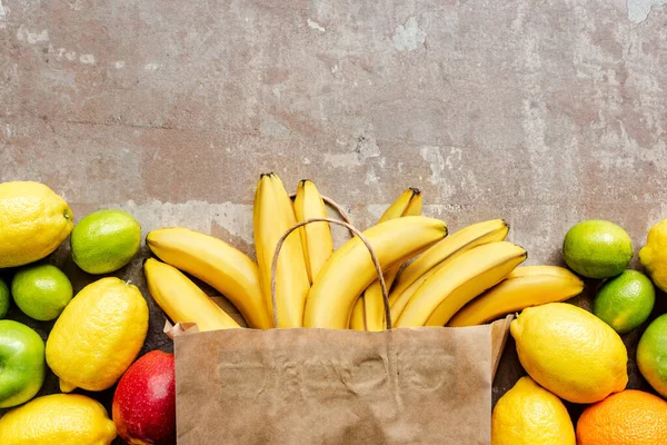 Top view of paper bag with colorful fresh fruits on beige weathered surface — Stock Photo