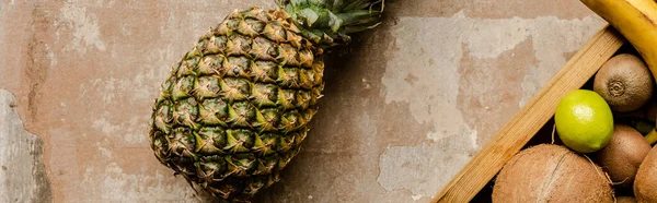 Top view of ripe pineapple near wooden box with fruits on weathered surface, panoramic crop — Stock Photo