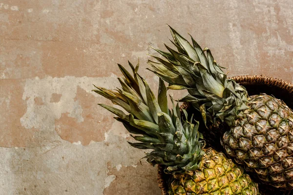 Top view of ripe exotic pineapples in wicker basket on weathered surface — Stock Photo