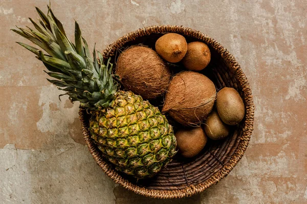 Vue de dessus des fruits exotiques mûrs dans le panier en osier sur la surface altérée — Photo de stock