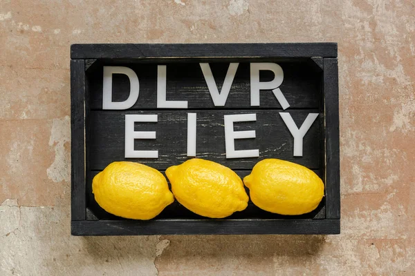 Vue du dessus de la livraison de mots près de citrons dans une boîte noire en bois sur une surface altérée — Photo de stock