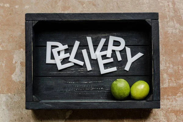 Top view of word delivery near limes in wooden black box on weathered surface — Stock Photo