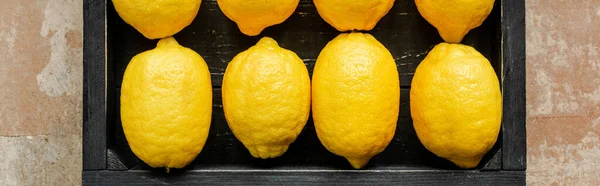 Vista superior de limones en caja negra de madera sobre superficie erosionada, cultivo panorámico - foto de stock