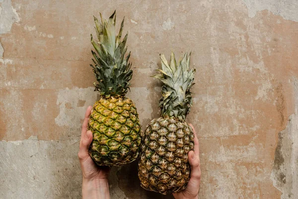 Cropped view of woman holding ripe pineapples on weathered surface — Stock Photo