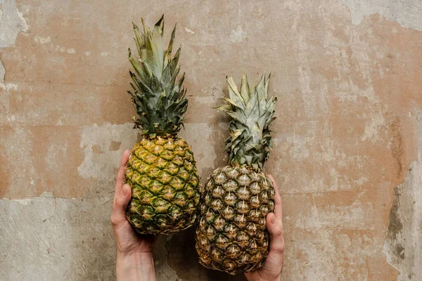 Vista ritagliata della donna che tiene gli ananas maturi sulla superficie alterata — Foto stock