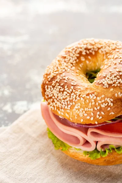 Fresh delicious bagel with sausage on napkin on textured surface — Stock Photo