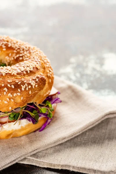 Rosquilla fresca deliciosa con carne, cebolla roja, queso crema y brotes en la servilleta en la superficie texturizada - foto de stock