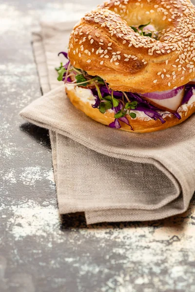 Fresh delicious bagel with meat, red onion, cream cheese and sprouts on napkin on textured surface — Stock Photo