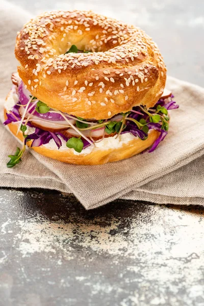 Rosquilla fresca deliciosa con carne, cebolla roja, queso crema y brotes en la servilleta en la superficie texturizada - foto de stock