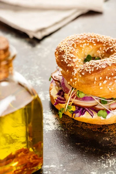 Selective focus of oil and fresh delicious bagel with meat, red onion, cream cheese and sprouts on textured surface — Stock Photo