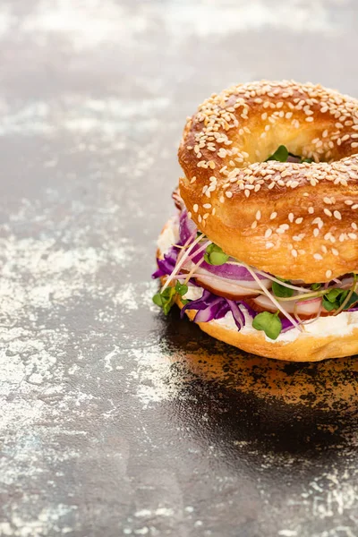 Fresh delicious bagel with meat, red onion, cream cheese and sprouts on textured surface — Stock Photo
