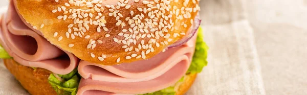 Bagel frais délicieux avec saucisse sur serviette sur surface texturée, vue panoramique — Photo de stock