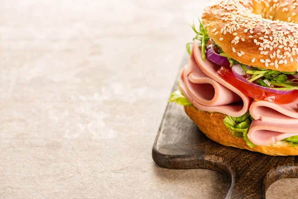 Fresh delicious bagel with sausage on wooden cutting board on textured surface — Stock Photo