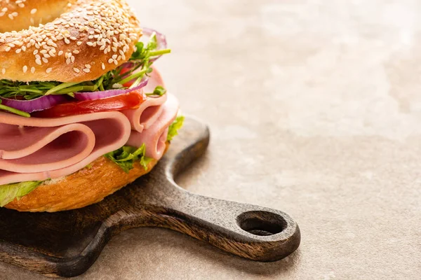 Fresh delicious bagel with sausage on wooden cutting board on textured surface — Stock Photo