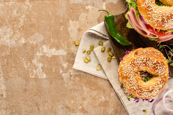 Top view of fresh delicious bagels on wooden cutting board on napkin with pumpkin seeds on aged beige surface — Stock Photo