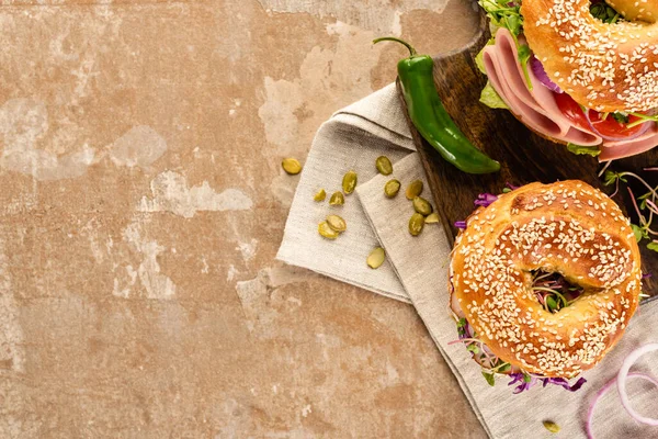 Vista dall'alto di deliziosi bagel freschi su tagliere in legno su tovagliolo con semi di zucca su superficie beige invecchiata — Foto stock