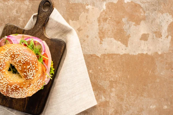 Vista dall'alto di deliziosi bagel freschi su tagliere in legno su superficie beige invecchiata con tovagliolo — Foto stock