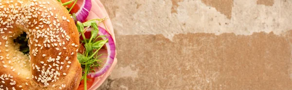 Draufsicht auf frischen leckeren Bagel mit Wurst auf gealterter beiger Oberfläche, Panoramaaufnahme — Stockfoto