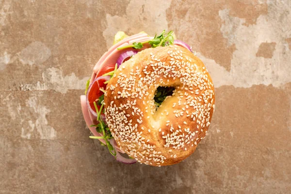 Top view of fresh delicious bagel with sausage on aged beige surface — Stock Photo