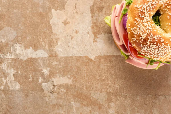 Top view of fresh delicious bagel with sausage on aged beige surface — Stock Photo