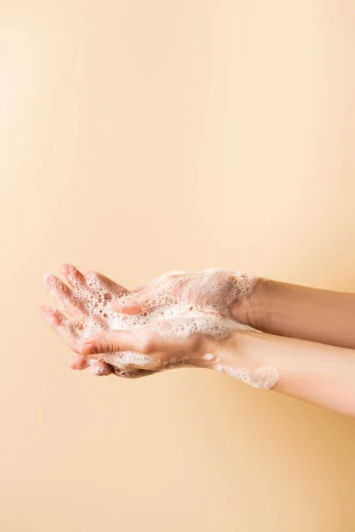 Vista recortada de las manos femeninas en espuma de jabón aislado en beige - foto de stock