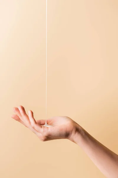 Vista cortada da mão feminina sob o fluxo de sabão líquido isolado em bege — Fotografia de Stock