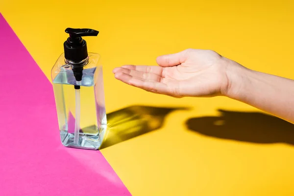 Partial view of female hand near bottle with disinfectant on pink and yellow — Stock Photo