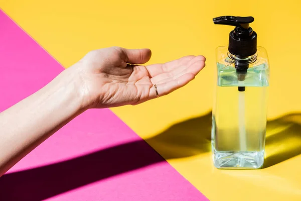 Vue recadrée de la main féminine près de la bouteille avec antiseptique liquide sur rose et jaune — Photo de stock