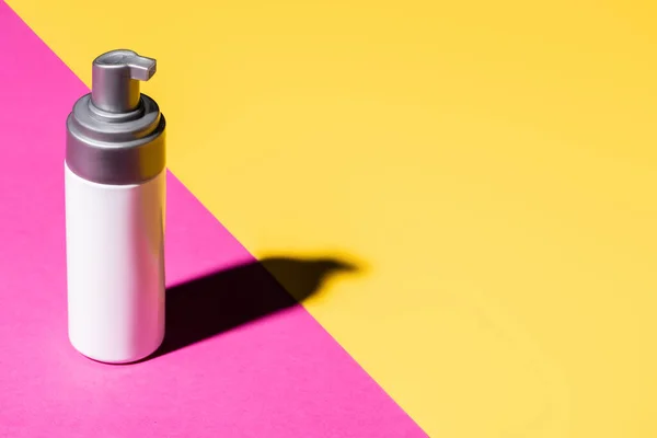 Container with cosmetic lotion on pink and yellow with shadow — Stock Photo