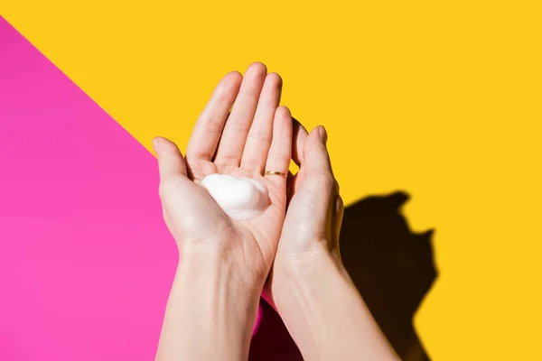 Vista parcial de las manos femeninas con espuma de jabón en rosa y amarillo - foto de stock