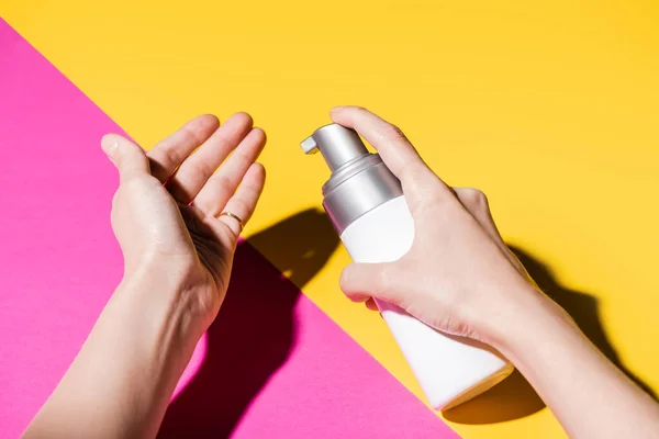 Partial view of woman applying hand lotion on pink and yellow — Stock Photo