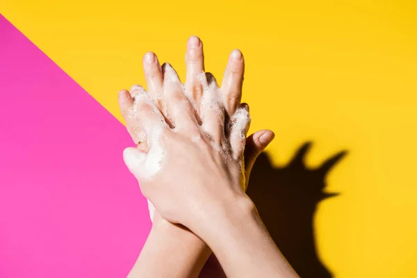 Vista ritagliata di donna che si lava le mani con schiuma di sapone su rosa e giallo — Foto stock