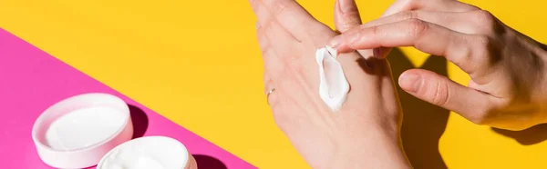 Cropped view of woman applying hand cream on pink and yellow, horizontal image — Stock Photo
