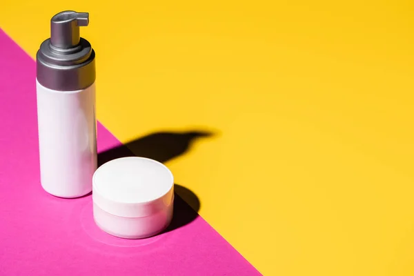 Dispenser with lotion and container with cosmetic cream on pink and yellow — Stock Photo