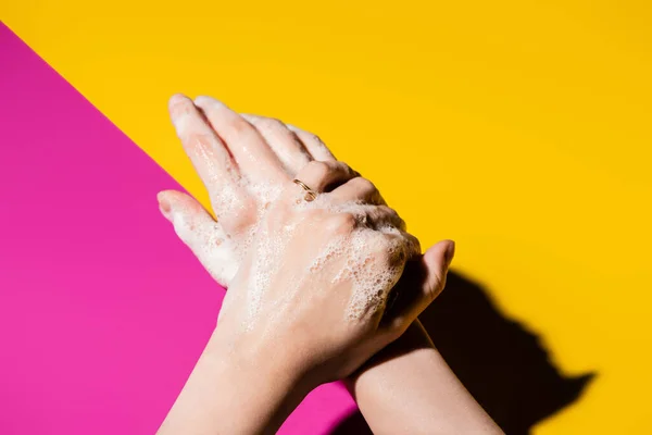 Vista parziale di donna che si lava le mani con schiuma di sapone su rosa e giallo — Foto stock