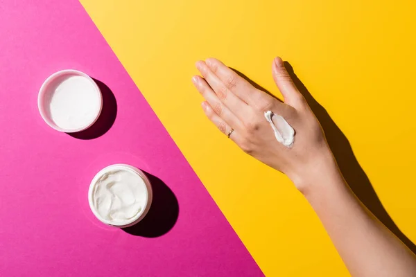 Partial view of female hand near container with hand cream on pink and yellow — Stock Photo