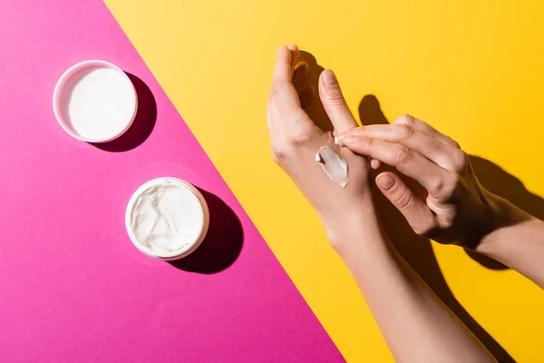 Vue recadrée de la femme appliquant crème pour les mains sur rose et jaune — Photo de stock