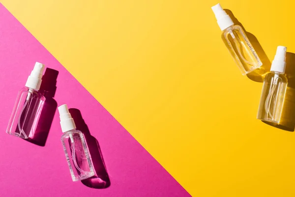 Вид зверху на прозорі пляшки спрею з антисептичною рідиною на рожевому і жовтому — стокове фото