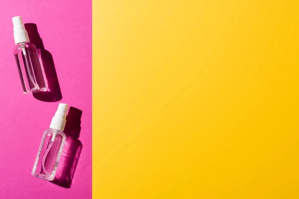 Top view of transparent spray bottles with sanitizer on pink and yellow — Stock Photo
