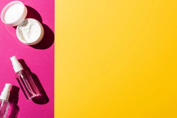Вид зверху пляшки спрею з антисептиком біля крему для рук на рожевому та жовтому — стокове фото