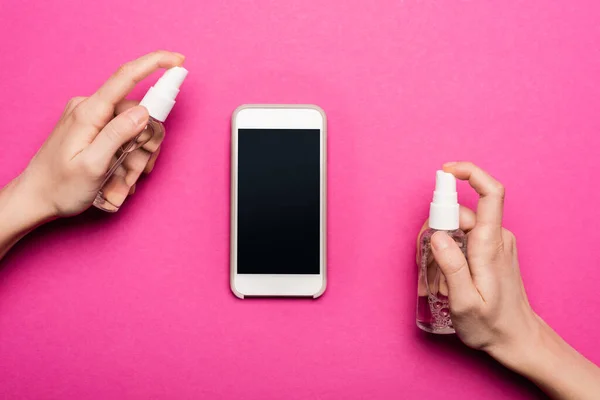 Teilbild einer Frau, die Antiseptikum auf Smartphone sprüht, mit leerem Bildschirm auf rosa — Stockfoto