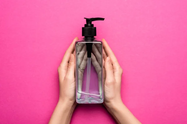 Обрезанный вид женских рук с бутылкой дезинфицирующего средства на розовом — стоковое фото