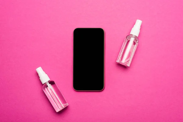 Vue du dessus des vaporisateurs avec liquide antiseptique près du smartphone avec écran blanc sur rose — Photo de stock