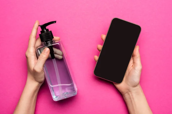 Vue recadrée de femme tenant désinfectant et smartphone avec écran blanc sur rose — Photo de stock