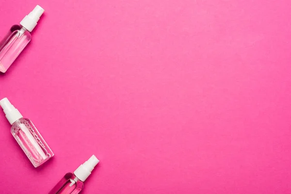 Вид сверху на прозрачные баллончики с дезинфицирующим средством для рук на розовом — стоковое фото
