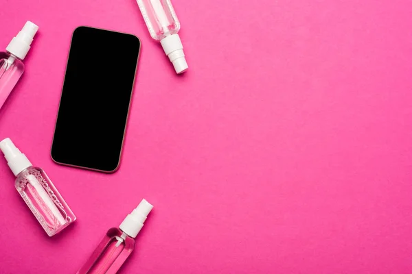 Vista dall'alto di bottiglie spray trasparenti con disinfettante vicino smartphone con schermo bianco su rosa — Foto stock