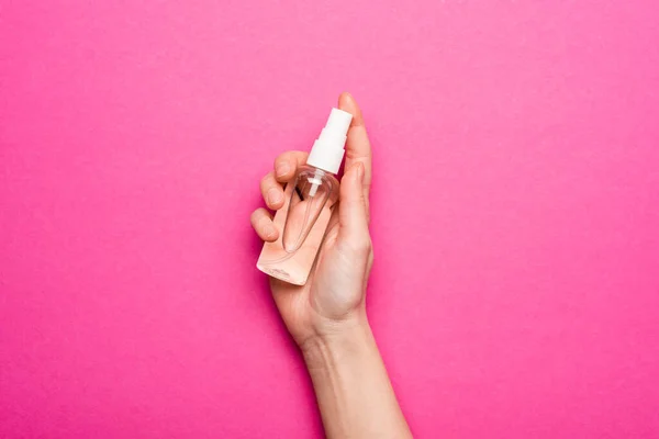 Teilansicht einer Frau mit transparenter Flasche mit Händedesinfektionsmittel auf rosa — Stockfoto